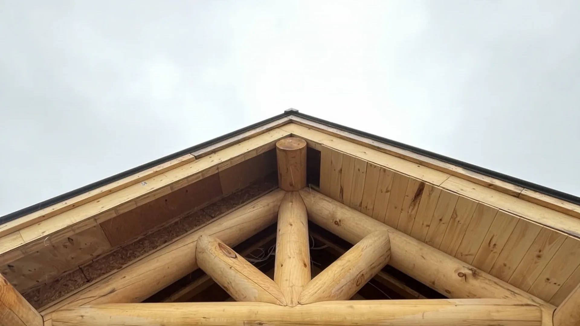 Charpente de bois massif apparente formant le pignon d’un toit sur mesure.