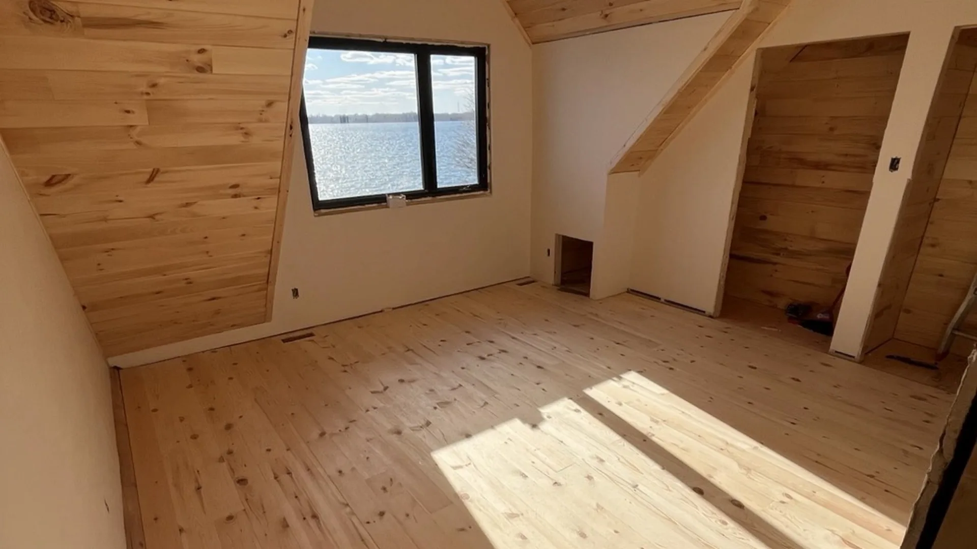 Pièce finie en bois clair, plafond cathédrale et fenêtre donnant sur le lac.